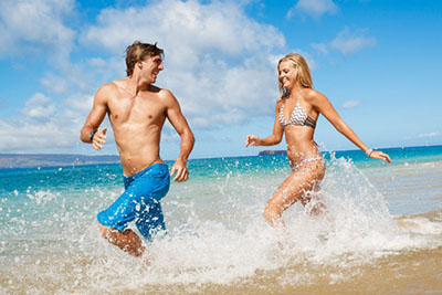 Couple running on beach with natural-looking golden tans